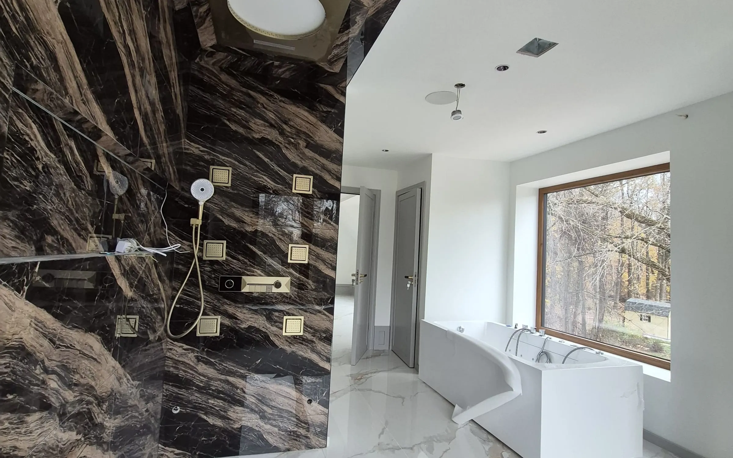 Bookmatched marble master bath — bookmatched marble shower wall, brass body sprays, freestanding tub