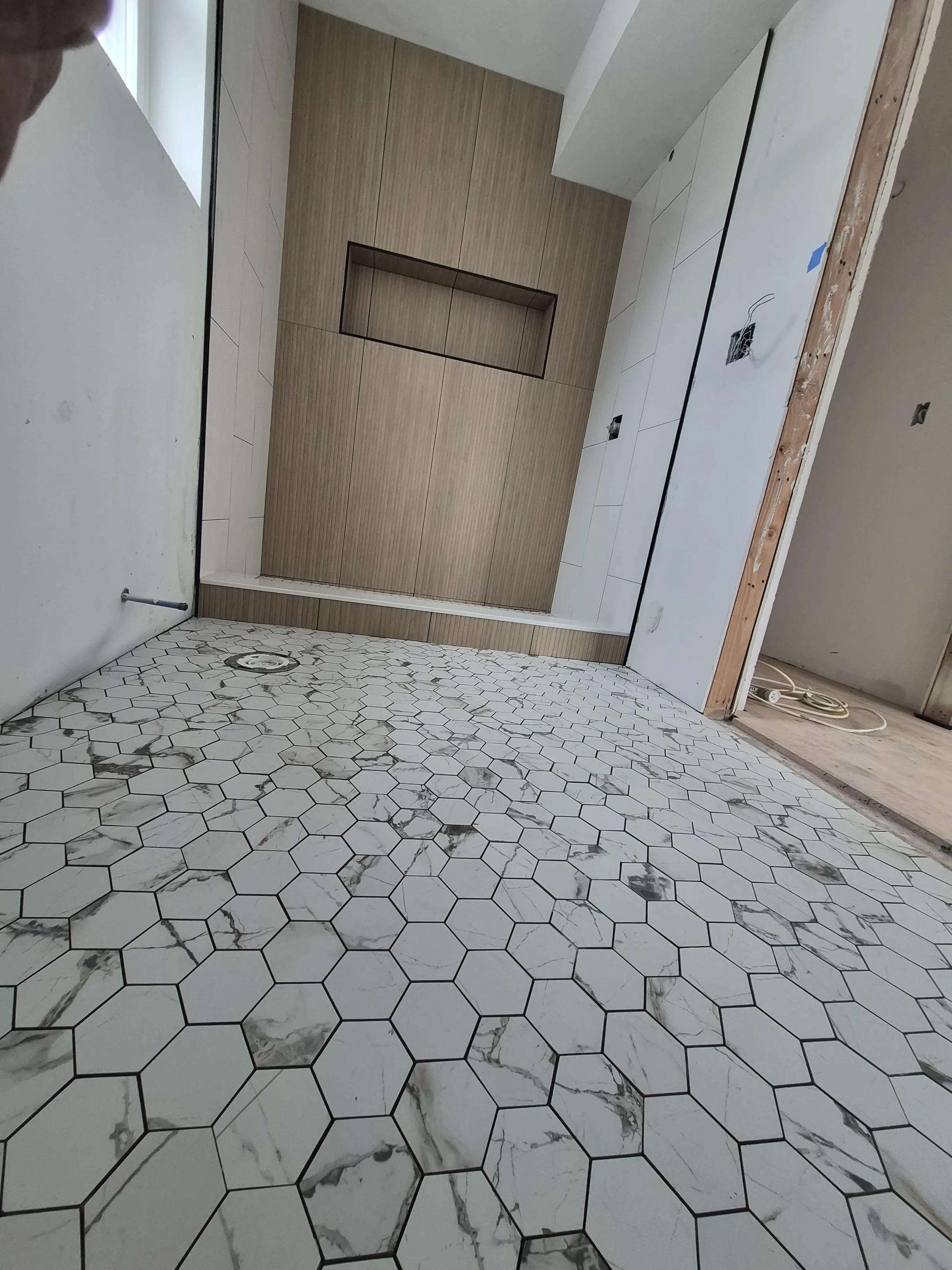 Walk-in wet room — wood-grain porcelain accent wall, hex marble floor, and recessed niche reference for bathroom tile installation